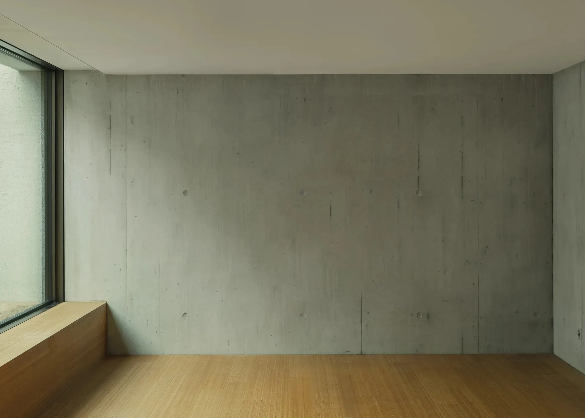 A minimalist interior with a concrete wall and wooden flooring.
