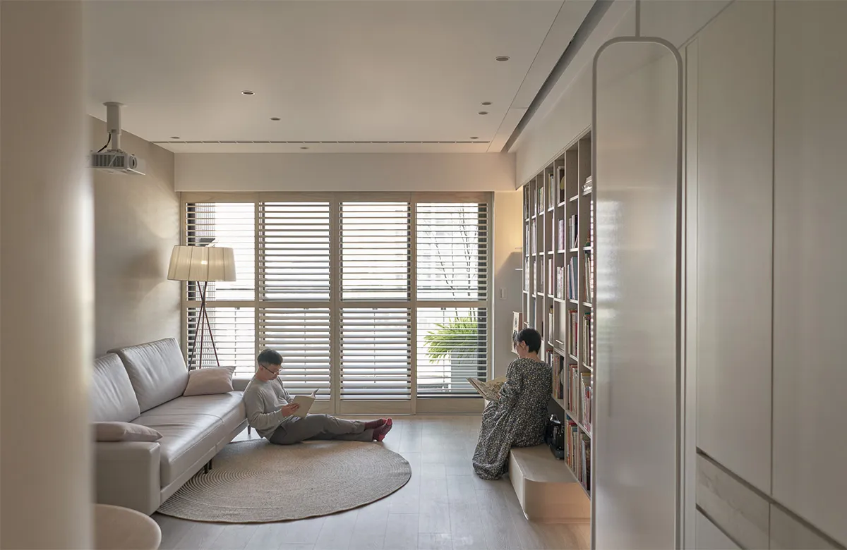 A minimalist living room featuring a white couch, glass shutters, and light wooden flooring.