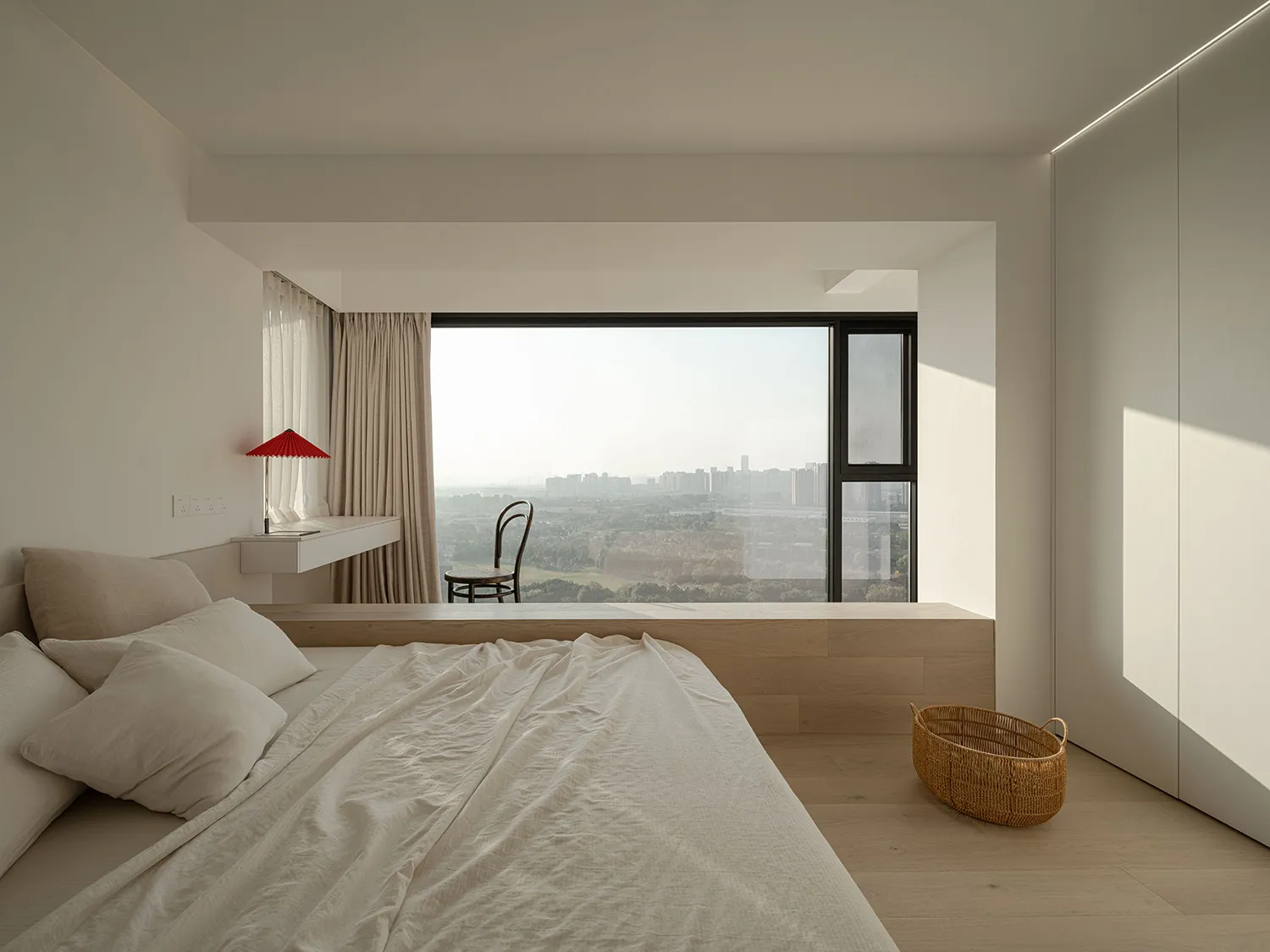 A modern bedroom featuring a large bed with a built-in desk and a cityscape view outside the window.