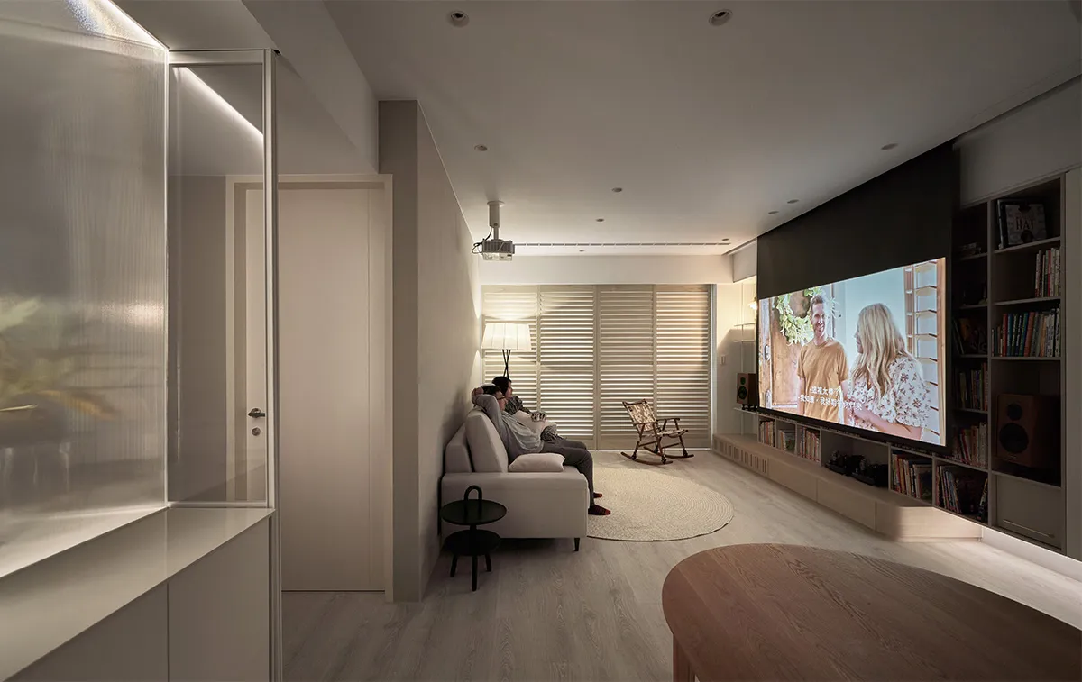 A modern living space featuring a white couch, large screen, and wooden coffee table in a room with neutral tones.