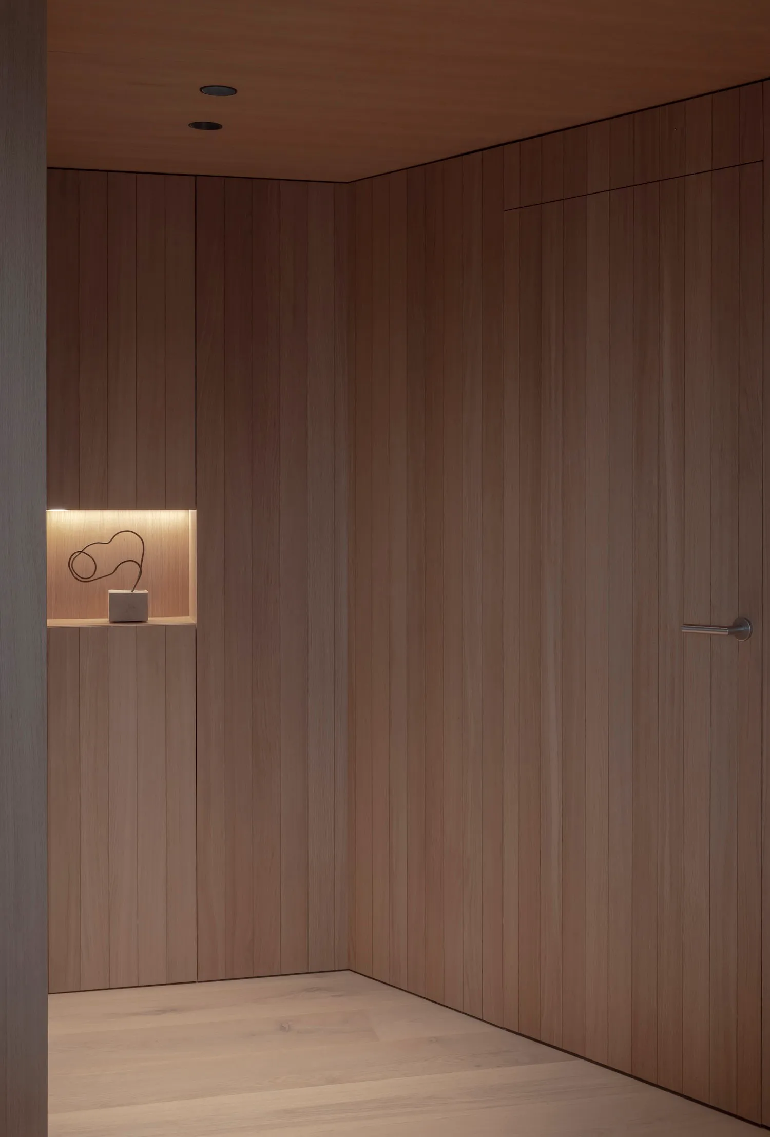 A minimalist closet with wooden panels and a small shelf with a sculptural object.