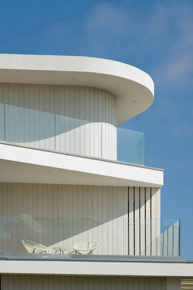Modern balcony featuring sleek white concrete and transparent glass barriers against a clear blue sky.