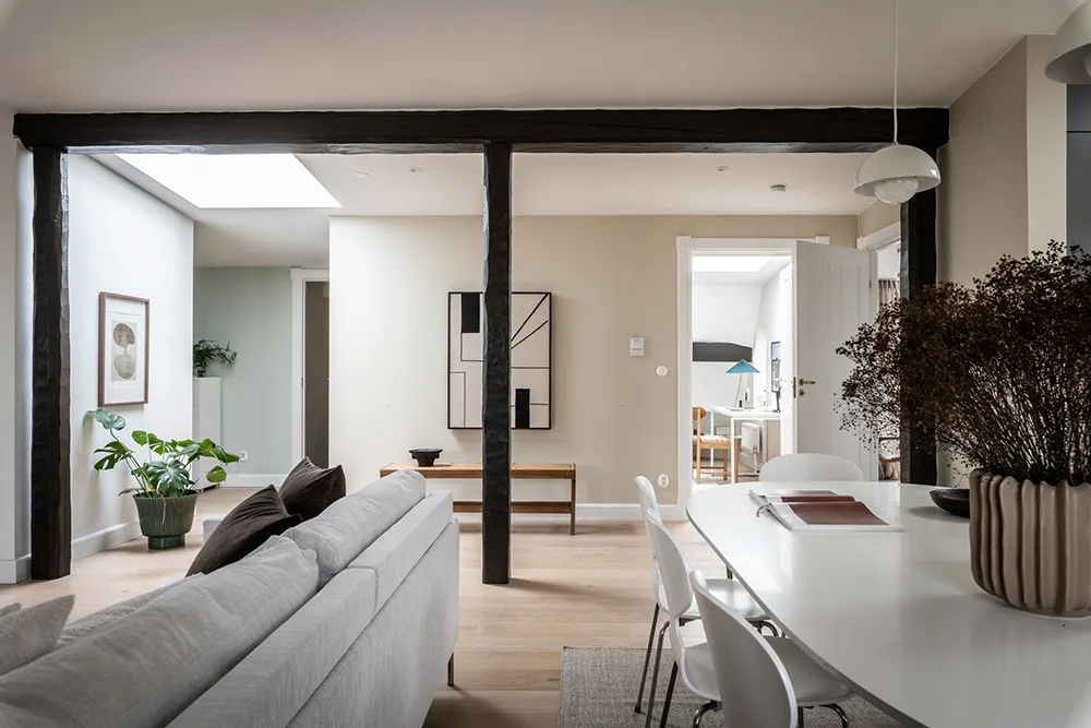 A modern living room featuring light wood flooring and white walls, with a comfortable seating area, dining table, and minima