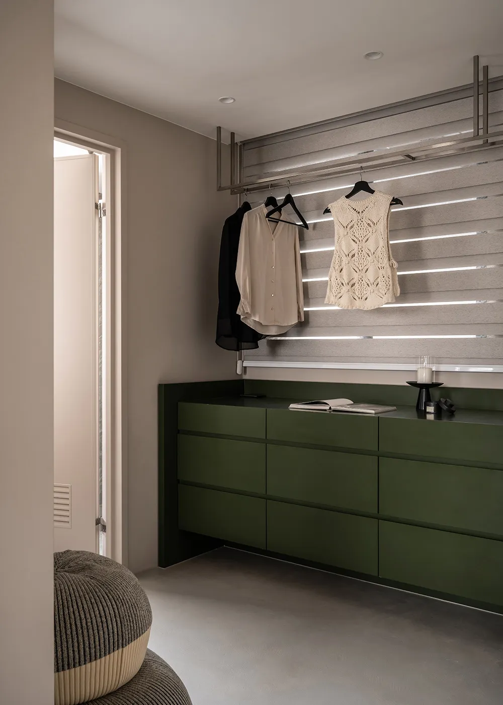 Modern minimalist clothes closet featuring metallic accents, green drawers, and clothes hanging on black hangers.