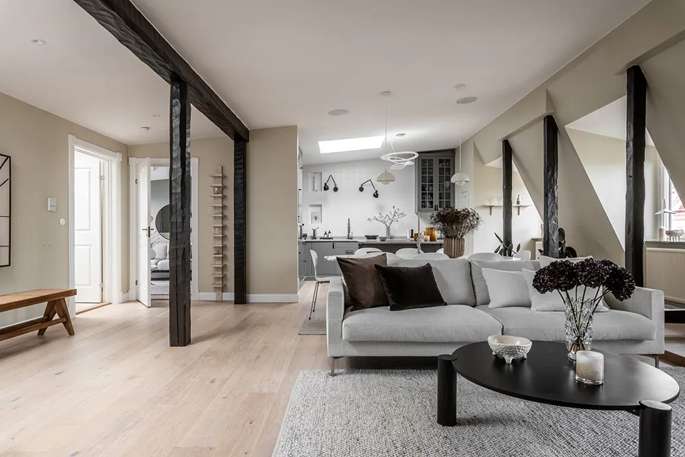 A minimalist living room featuring concrete walls, wooden furniture, and a grey sofa with black pillows.