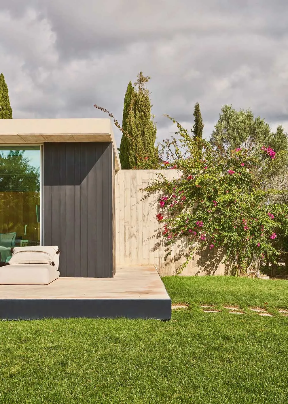 A minimalistic house with a concrete patio and greenery in the background.
