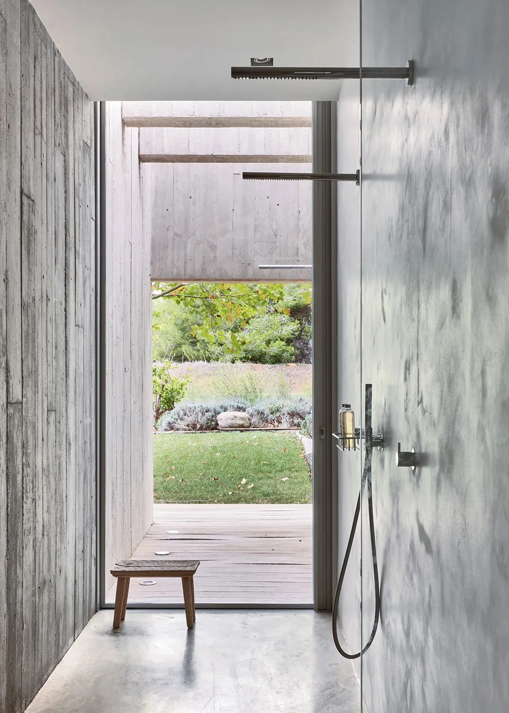 Modern bathroom with concrete walls and floor, featuring a walk-in shower with a view of the outdoor patio