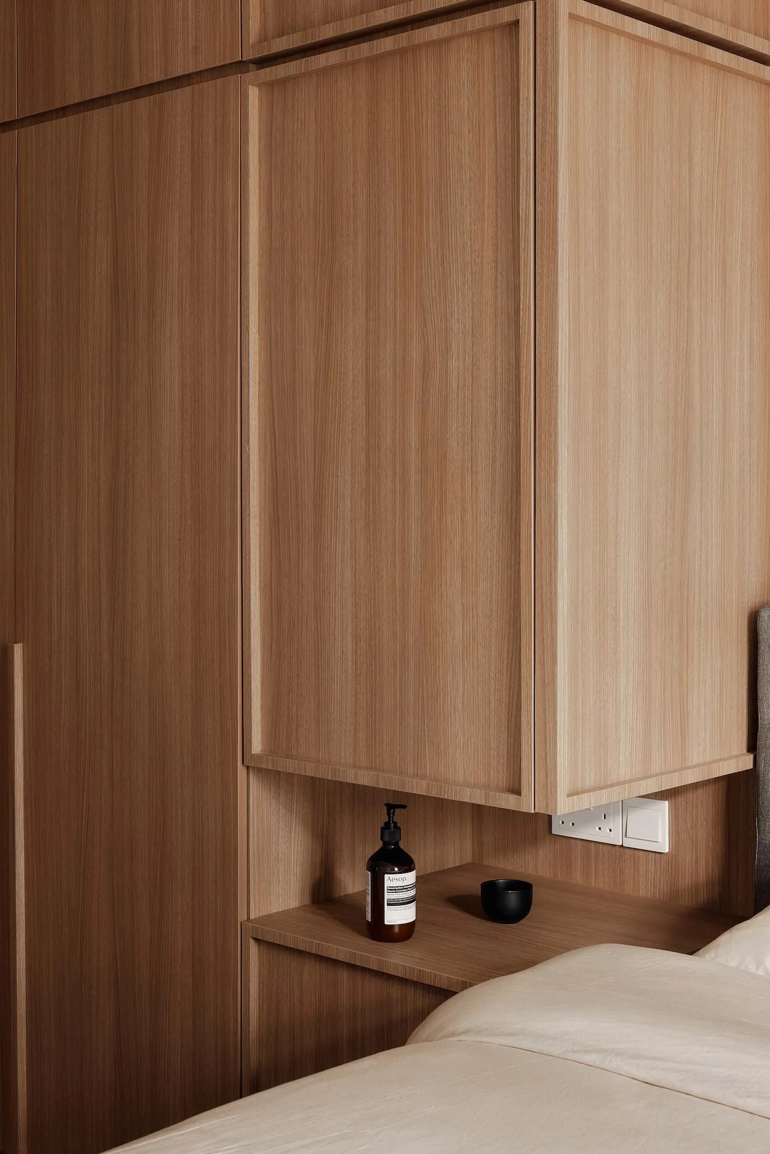 A modern bedroom featuring a wooden cupboard with built-in shelves and a black bottle of lotion.