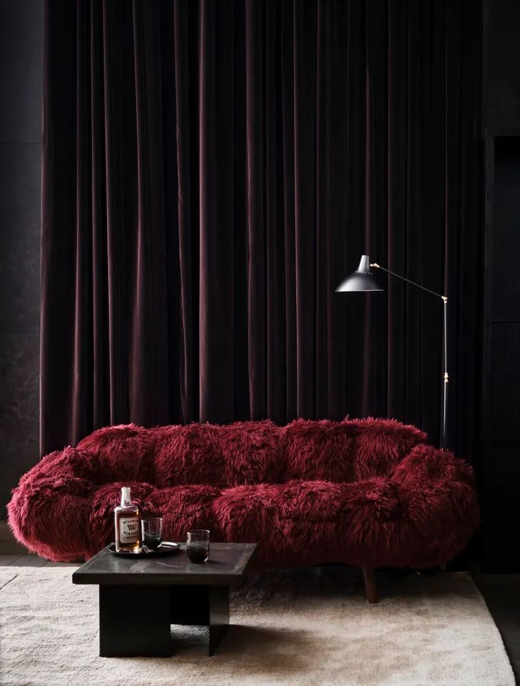A modern living room featuring a plush, burgundy velvet couch, a black coffee table with a whiskey bottle and glasses, and a
