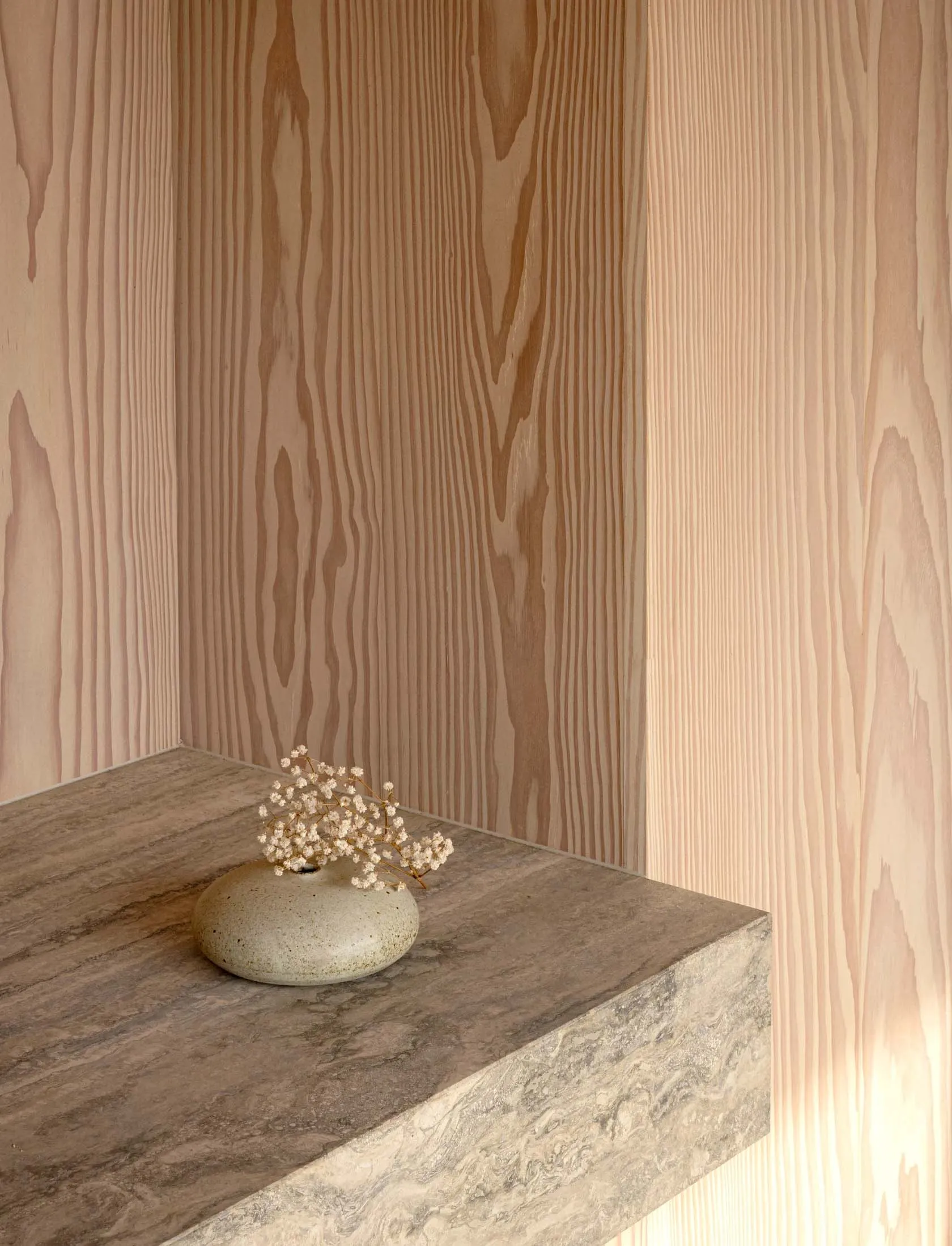 A ceramic vase with small white flowers on a wooden shelf.