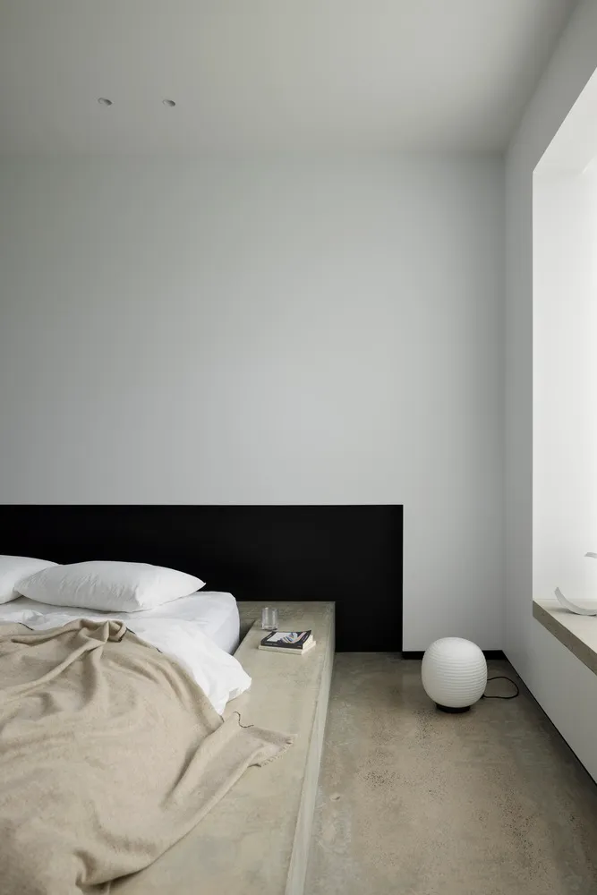 A minimalist bedroom with a concrete floor, wood headboard, and clean, simple design.