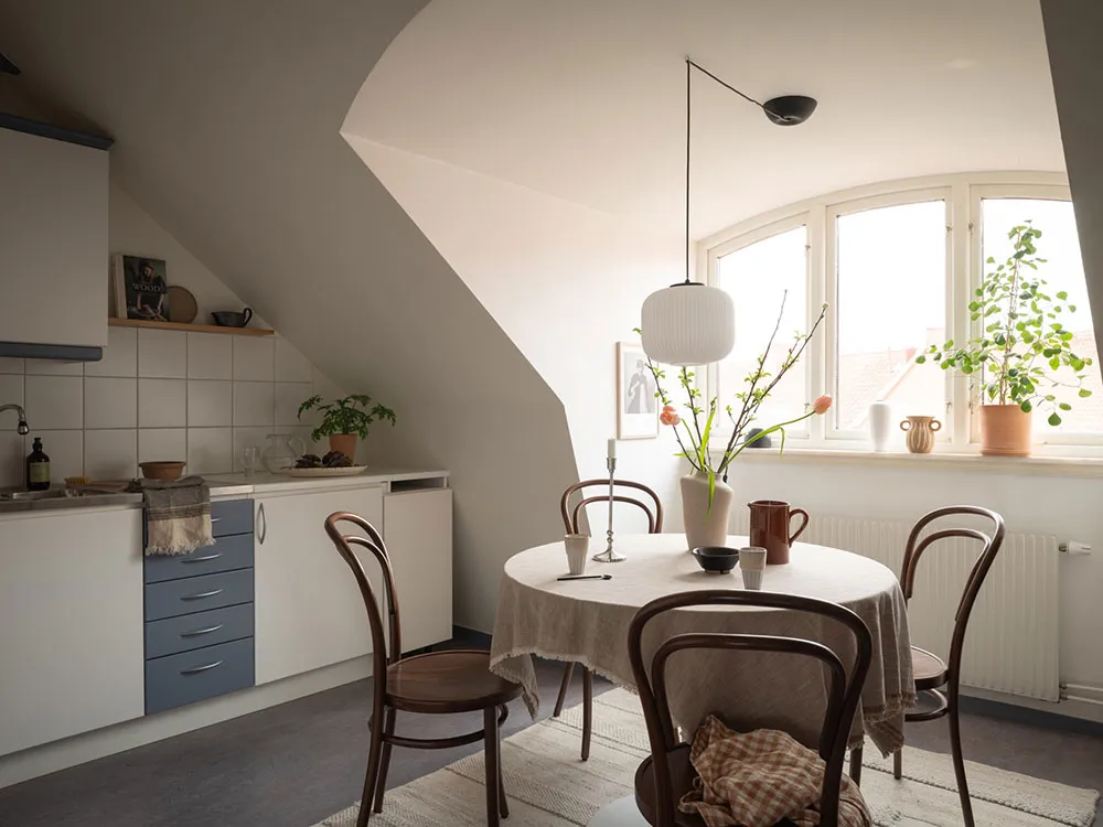 A minimalist kitchen with wooden furniture, a round table, and a window with greenery.