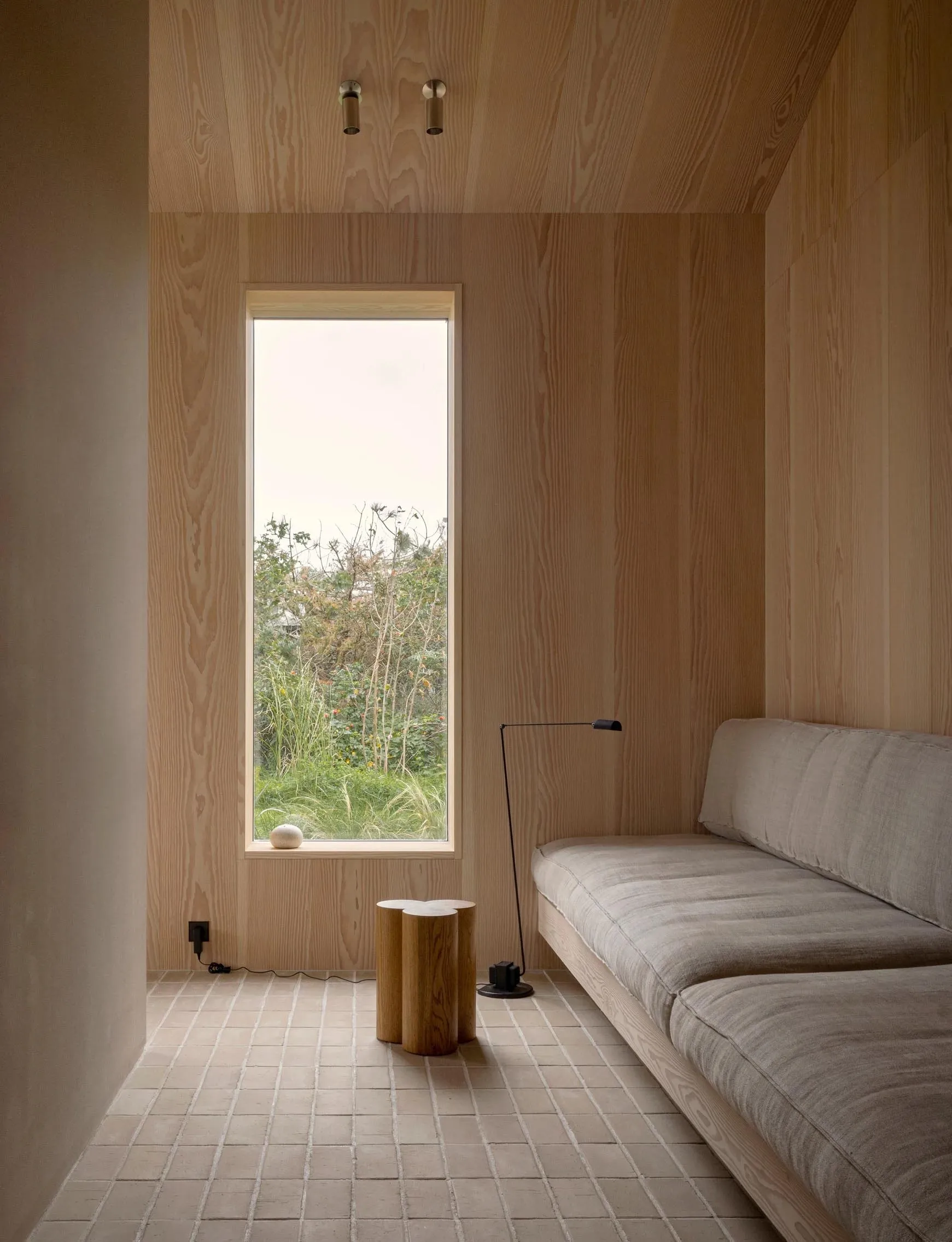 A minimalist living space featuring a concrete floor, wooden walls, and a small sofa with a floor lamp.