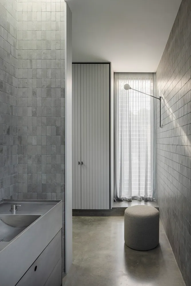 A modern bathroom featuring concrete-tiled walls and flooring, with a concrete sink and minimalist design elements.
