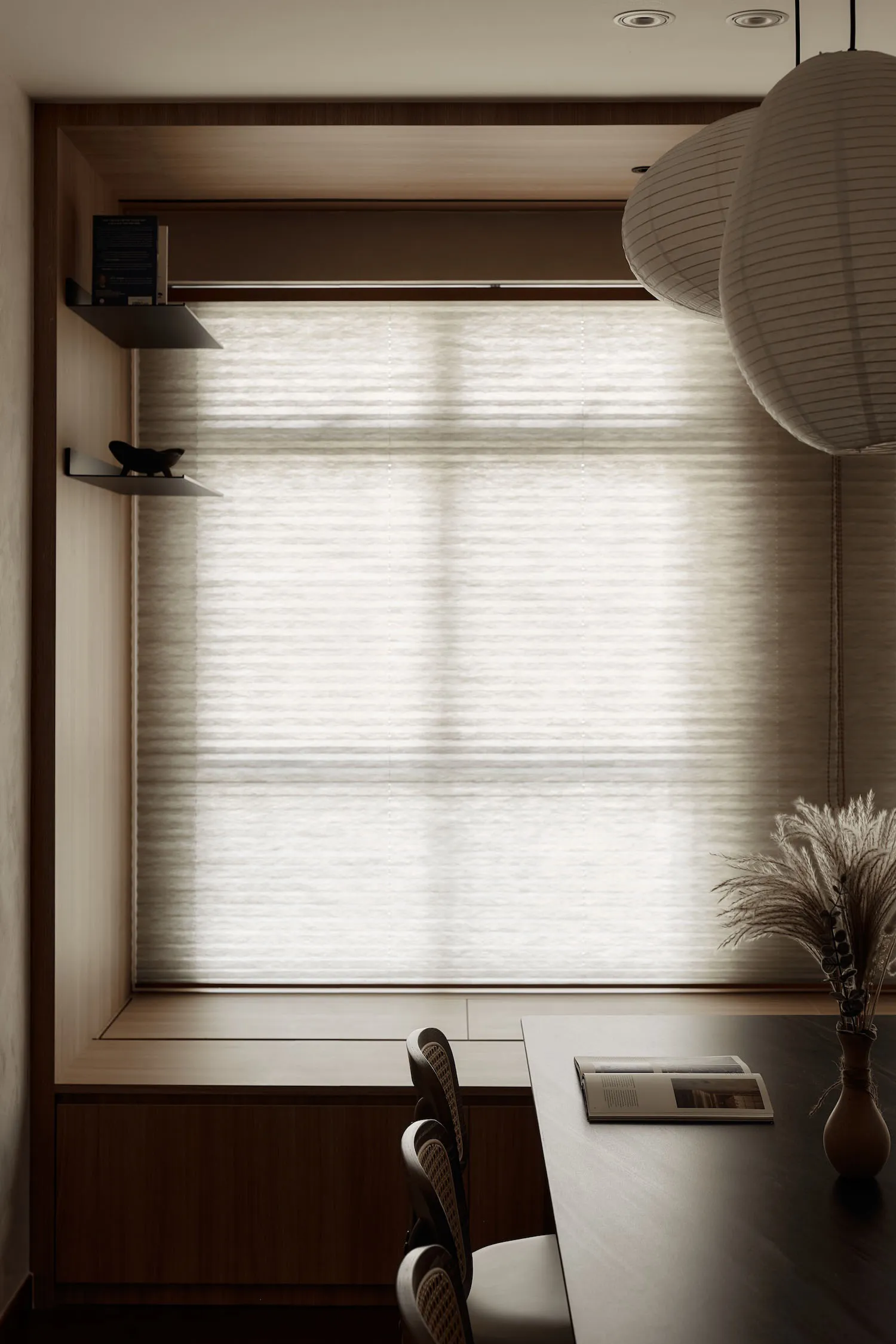 A minimalist interior space featuring a window seat with textured wood seating and fabric blinds.