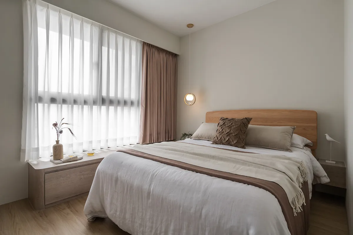 A minimalist bedroom with a light-colored bed, white and brown curtains, and a wooden headboard.