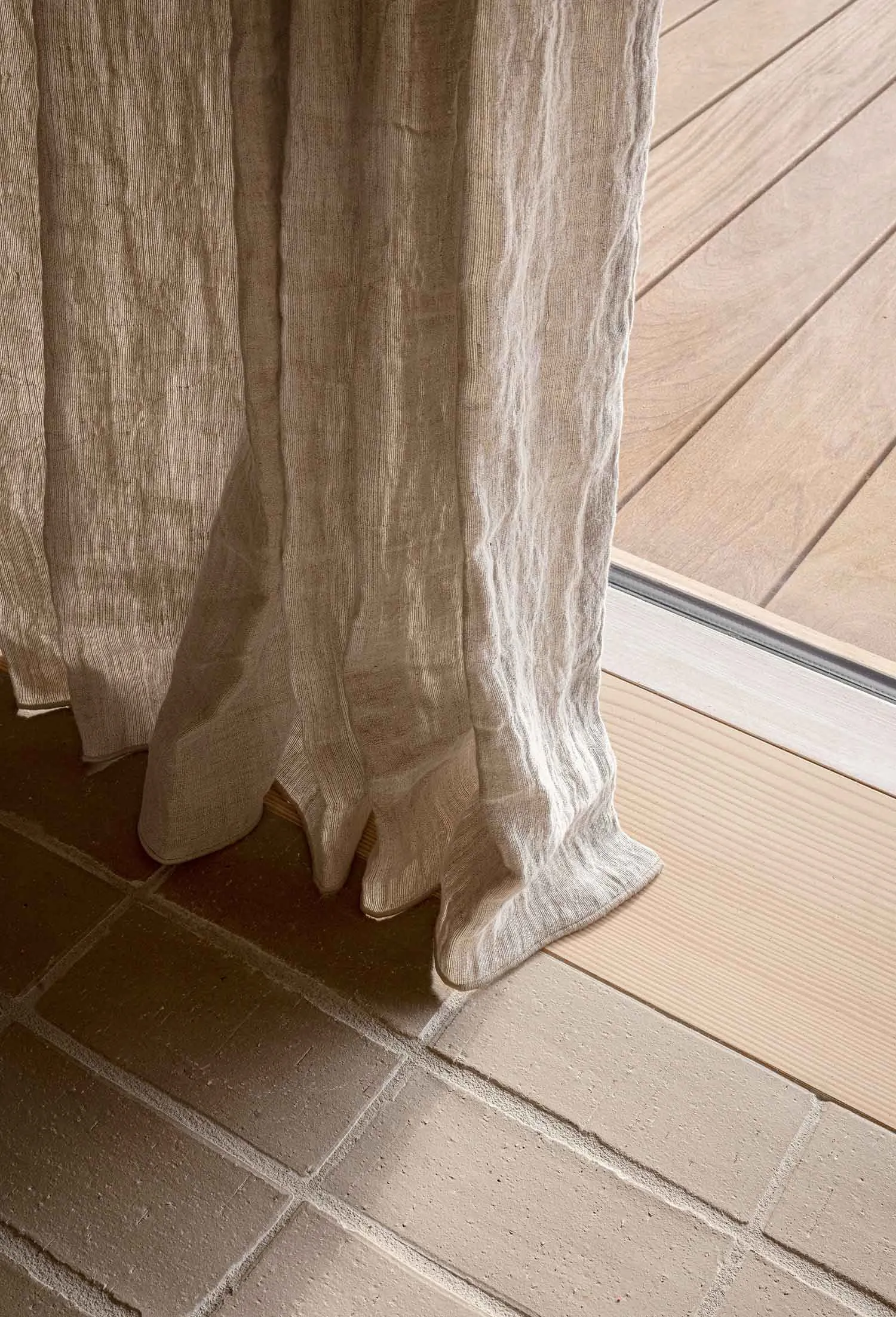 Lightweight textured linen curtains with a subtle striped pattern hanging in a natural wooden floor setting.