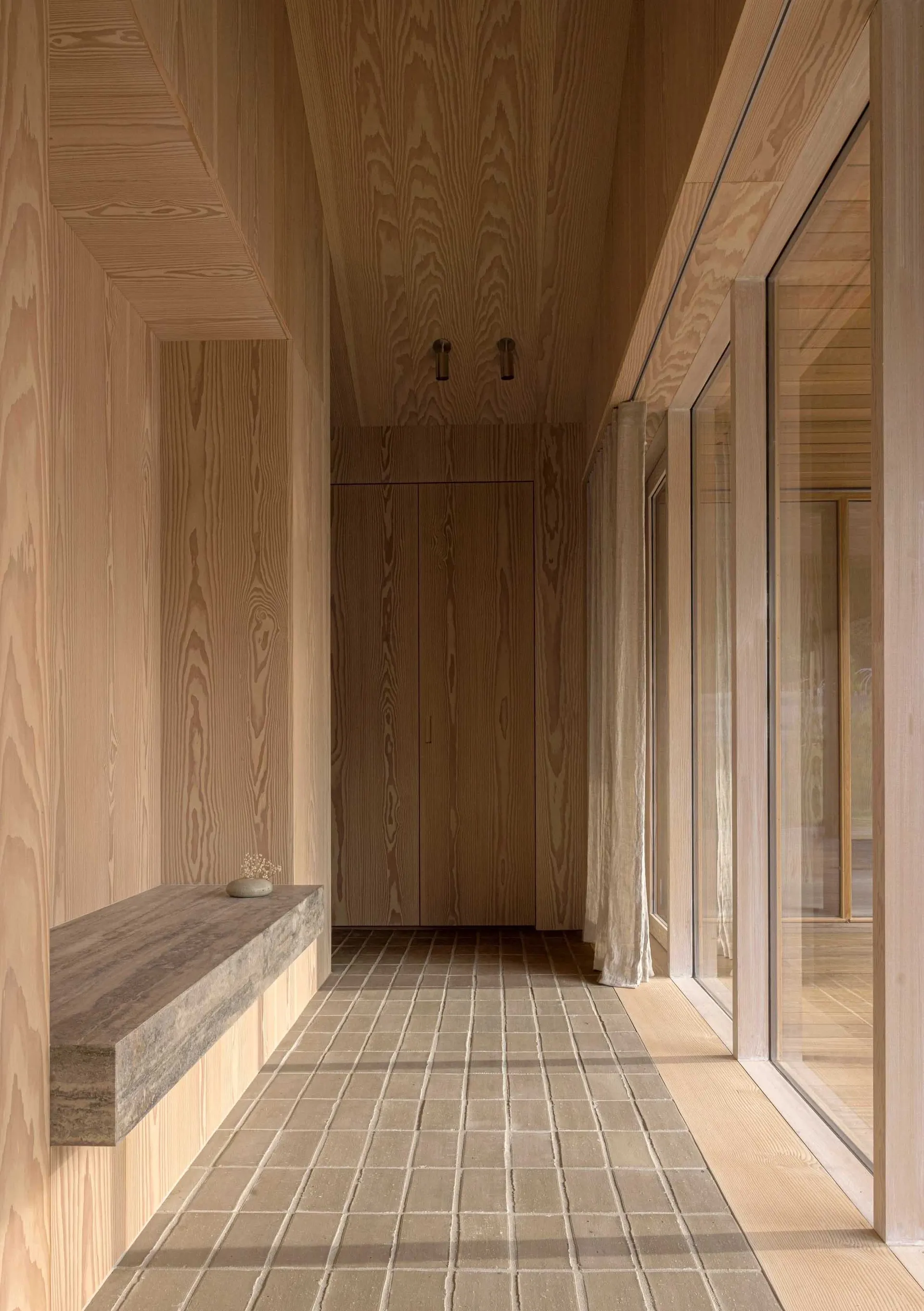 A modern wooden hallway with a tiled floor and a floating concrete bench.