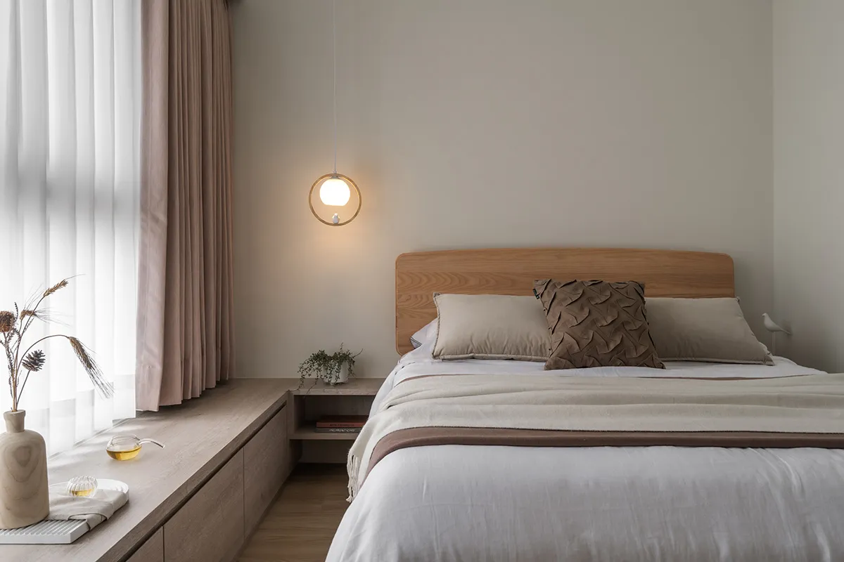 Minimalist bedroom featuring a wooden bed with beige bedding and curtains, a round pendant light, and a wooden window sill wi