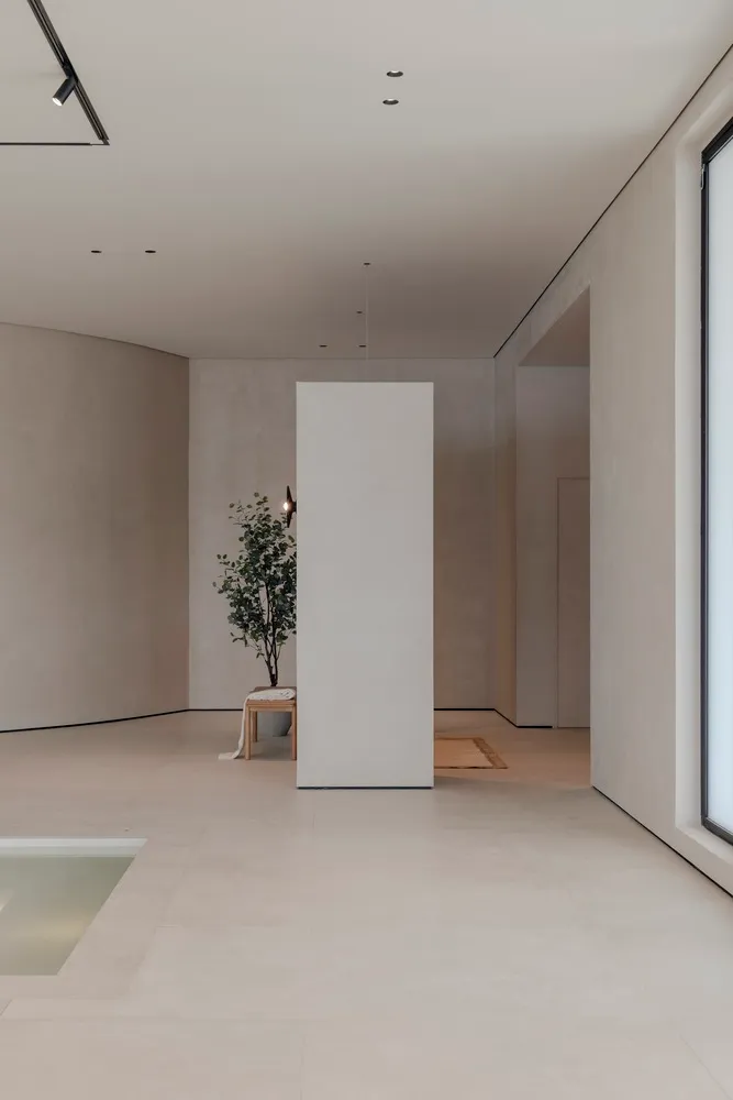A minimalist interior space with a white column, grey walls, and a small green plant in a vase on a table.