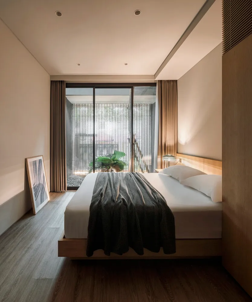 A modern bedroom with a wooden floor, a bed covered with a striped blanket, and a framed artwork leaning against the wall.