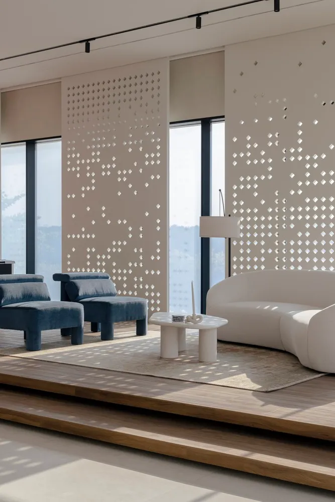 Modern living room featuring white curved sofa, blue upholstered chairs, wooden steps, and large windows with geometric wall