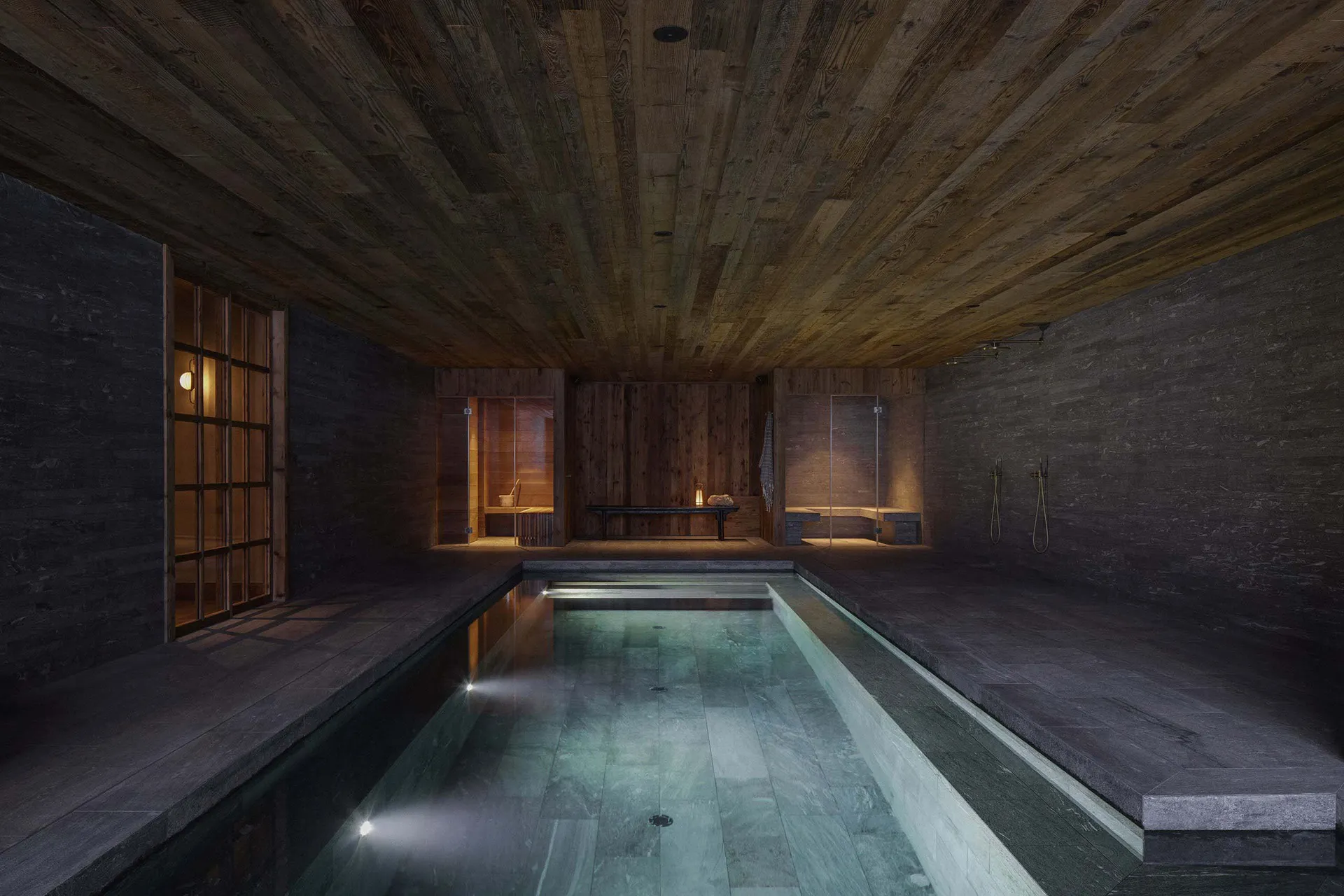 A minimalist spa interior featuring stone walls and flooring, with a small indoor pool and seating areas.