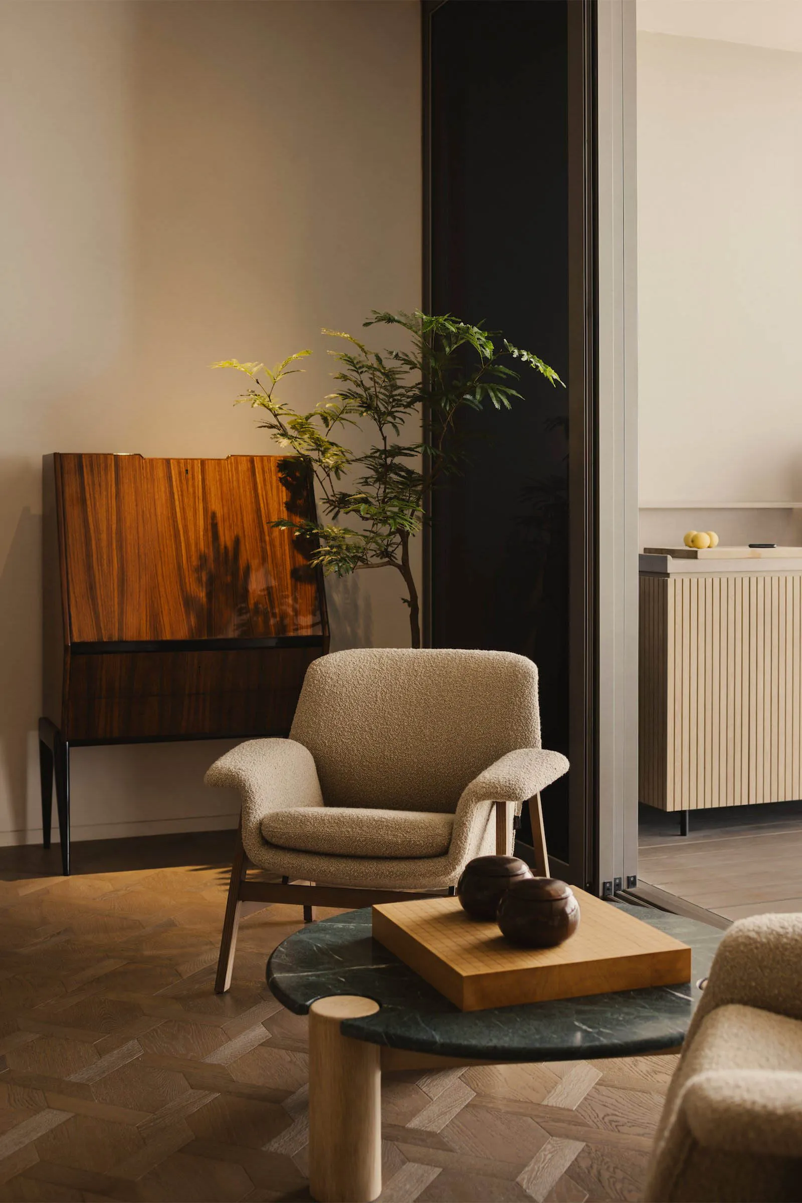 A modern living room featuring a beige textured armchair, a green marble coffee table, and a wooden cabinet with a plant。