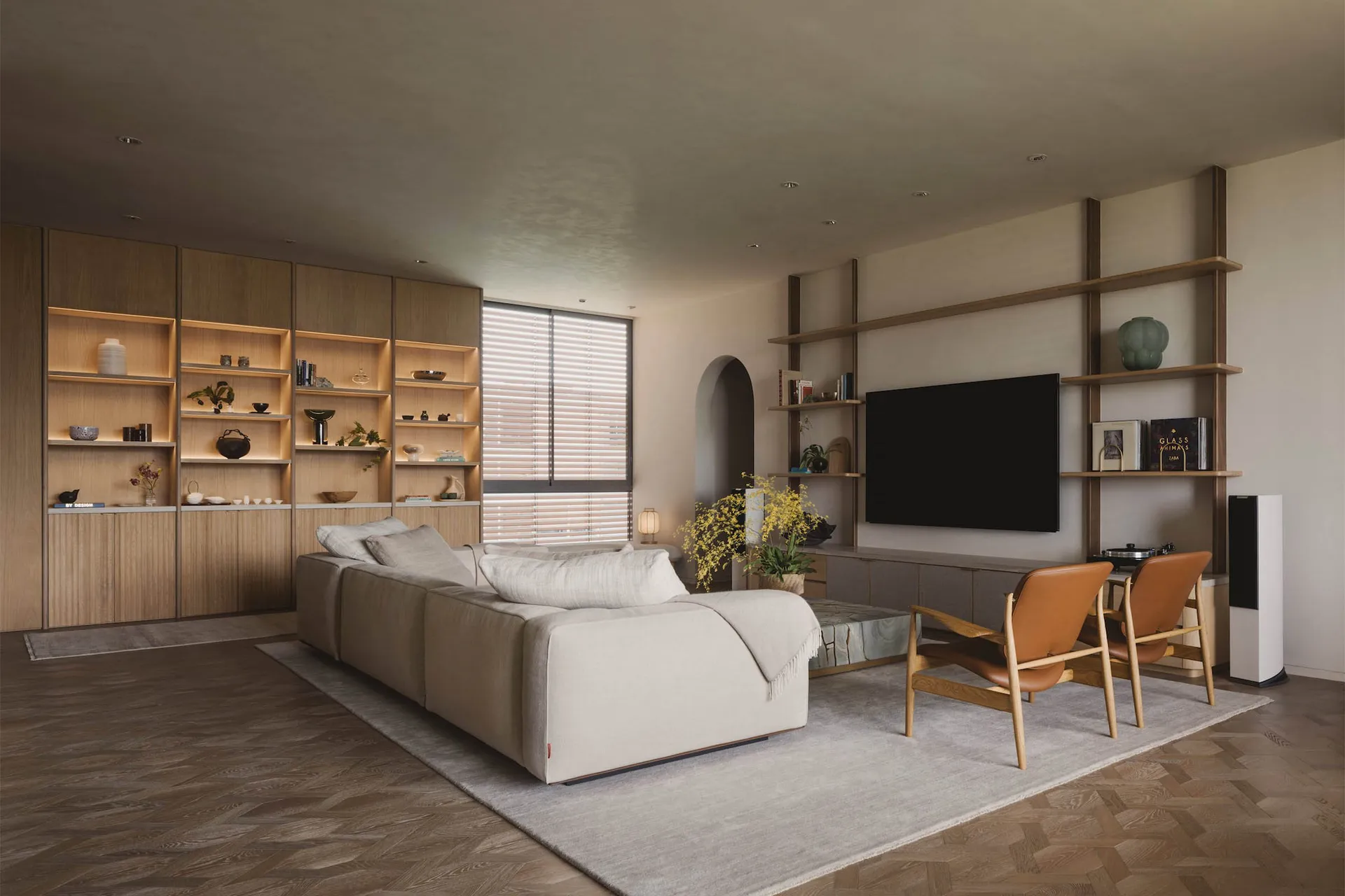 A modern living room with a grey sofa, wooden shelves, and a large window with blinds.