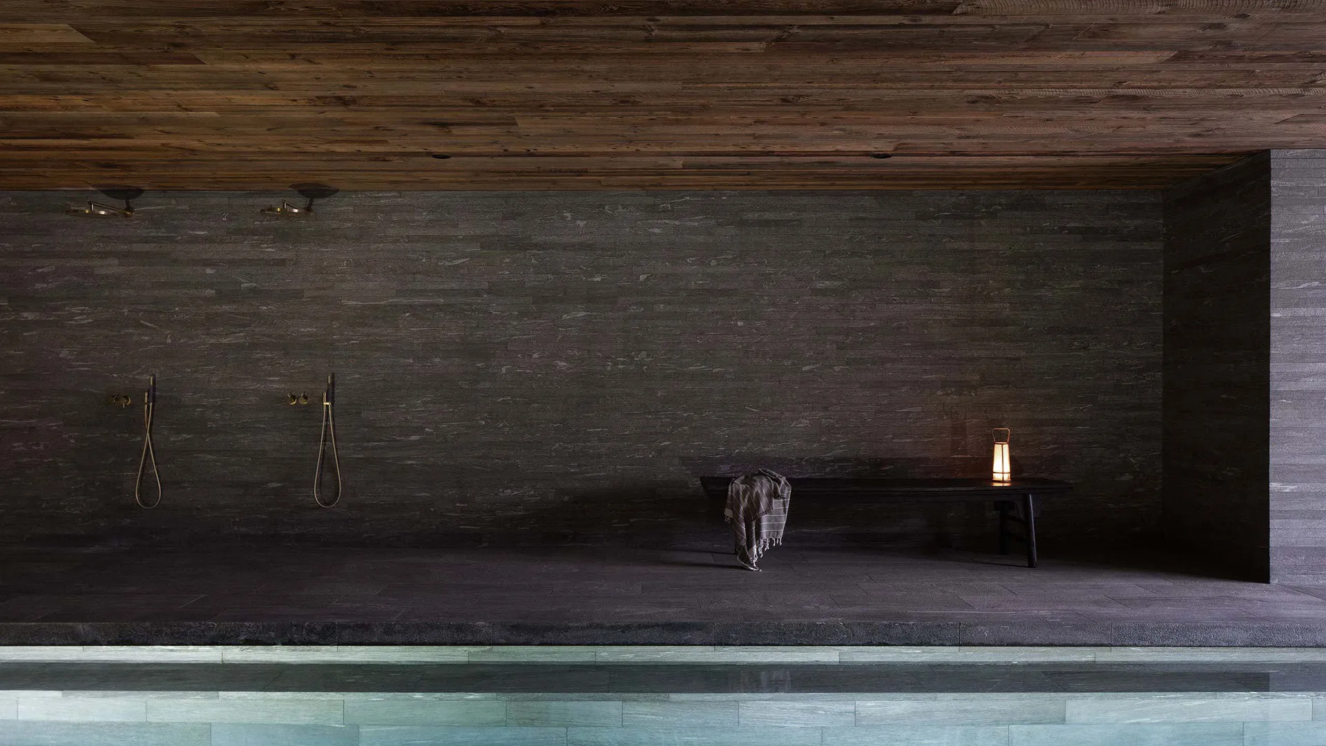 A serene spa poolside relaxation area with granite and stone walls, wood flooring, and a lantern.