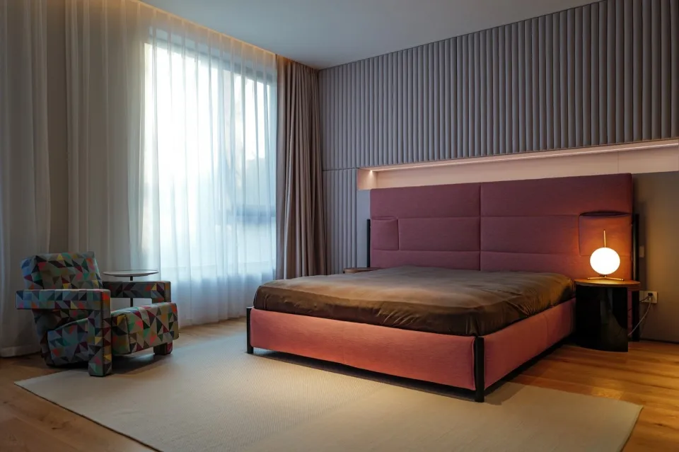 Interior design of a minimalist bedroom featuring a bed with a large burgundy headboard and an armchair with a geometric prin