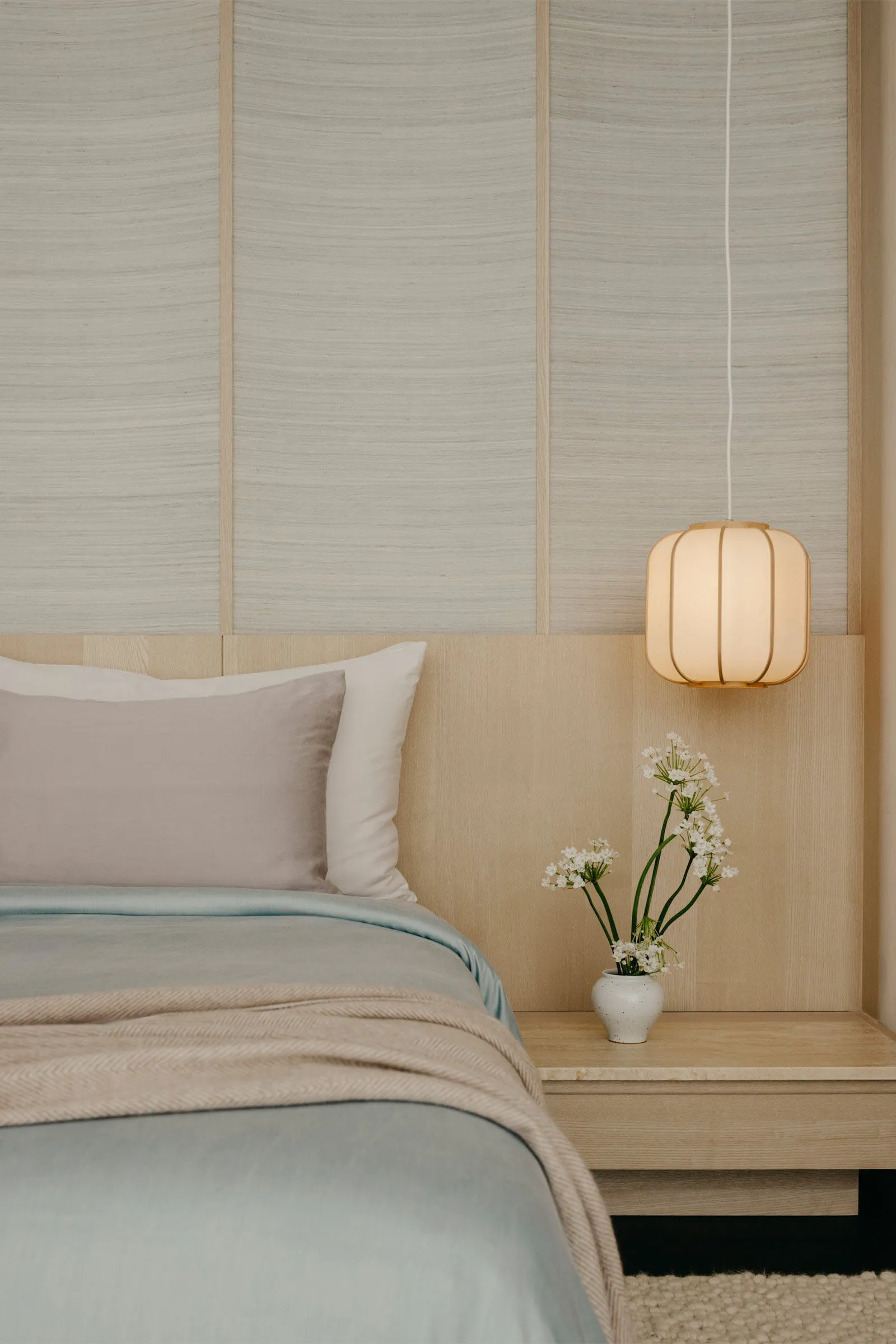 A minimalist bedroom with a bed, pillows, and a hanging lamp with flowers on a nightstand.