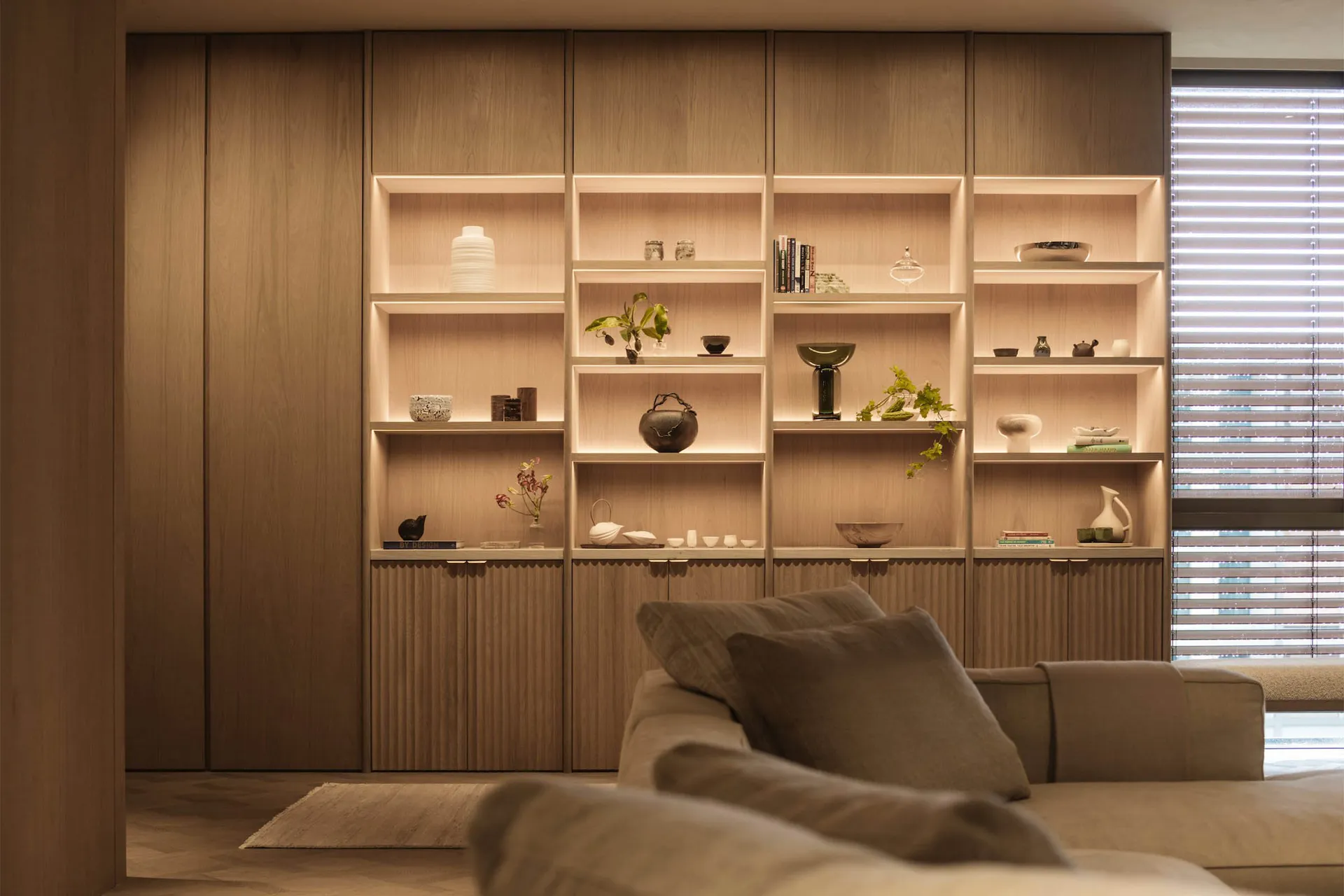 A modern minimalist living room with wooden shelves displaying decorative items and books.