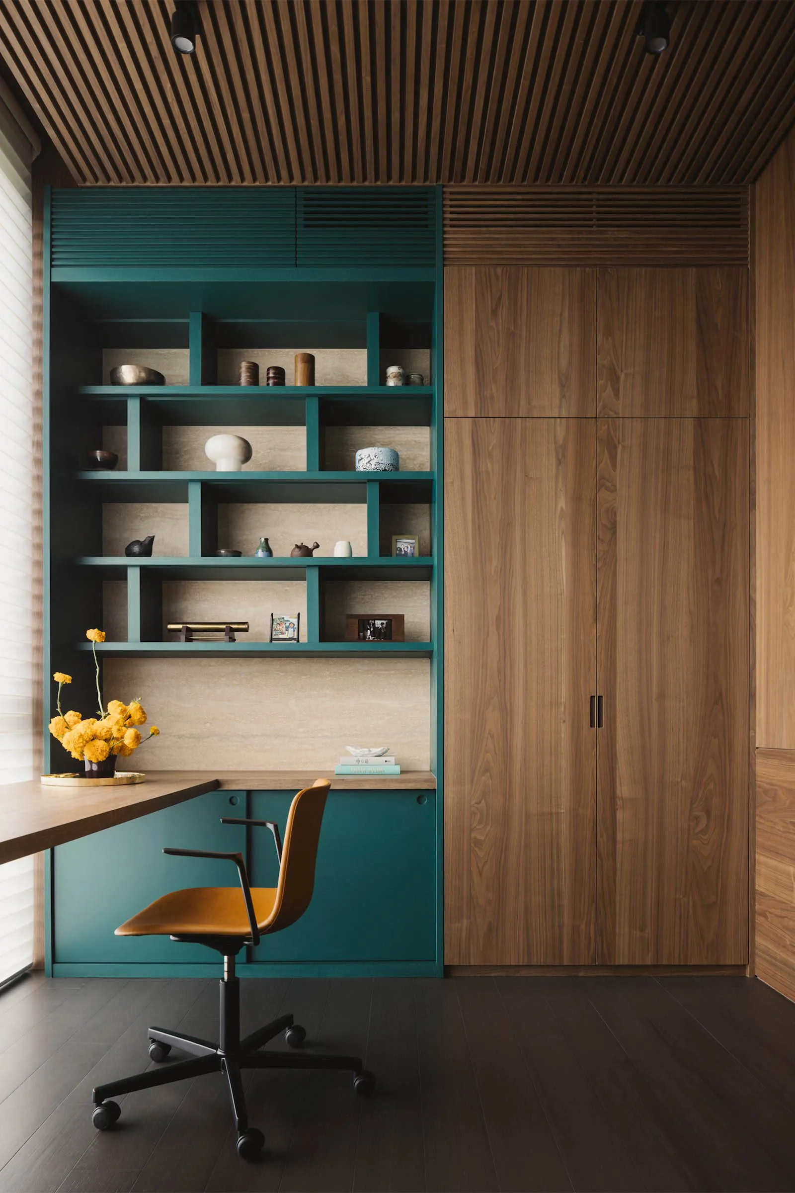 A modern home office featuring a teal storage unit and wooden paneling.