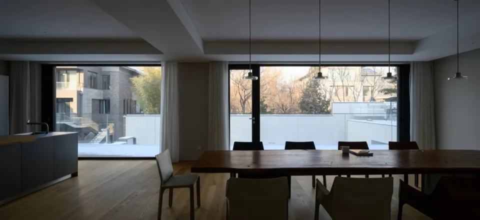 Modern residential dining room featuring a wooden dining table and glass walls overlooking a snowy courtyard.
