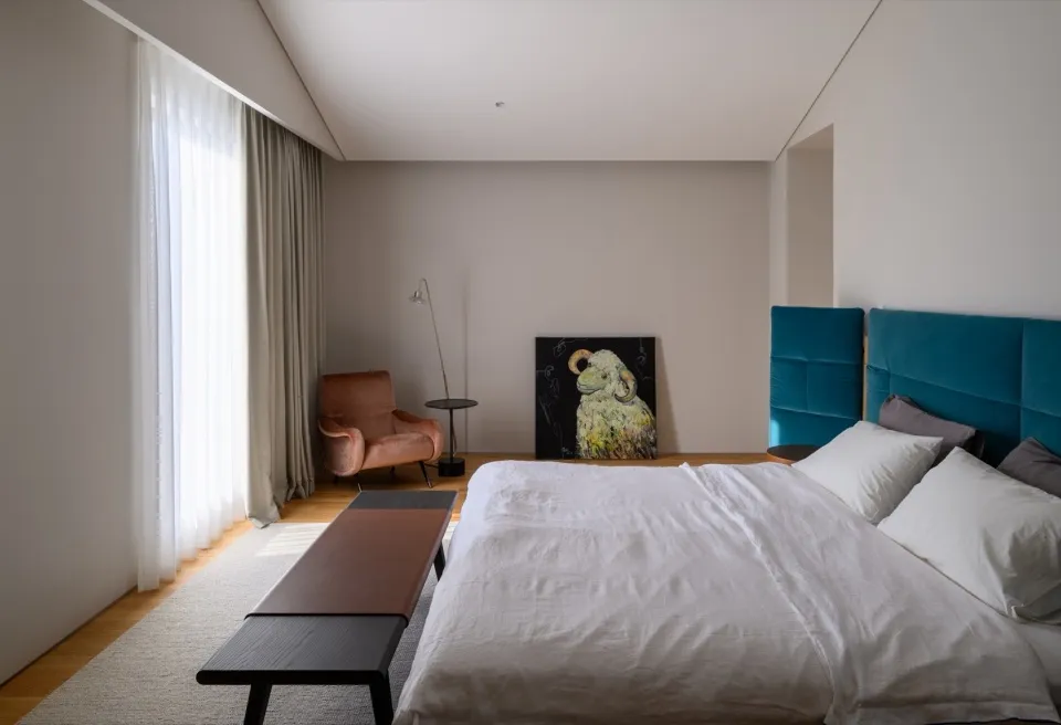 A minimalist bedroom with a blue velvet headboard, white bedding, and a textured wool floor.