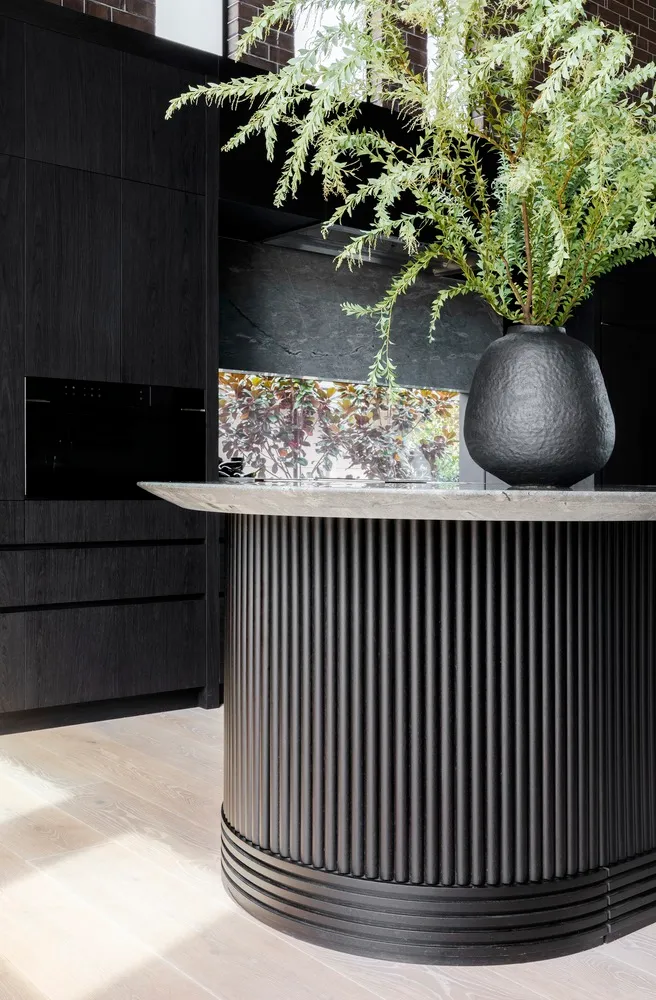 Modern minimalist black kitchen with stone countertops and green foliage in a vase.