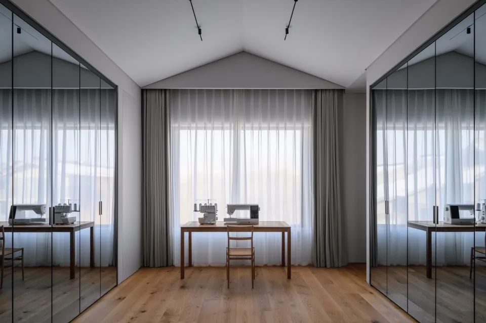 A minimalist workspace with wooden furniture, glass windows, and fabric curtains.