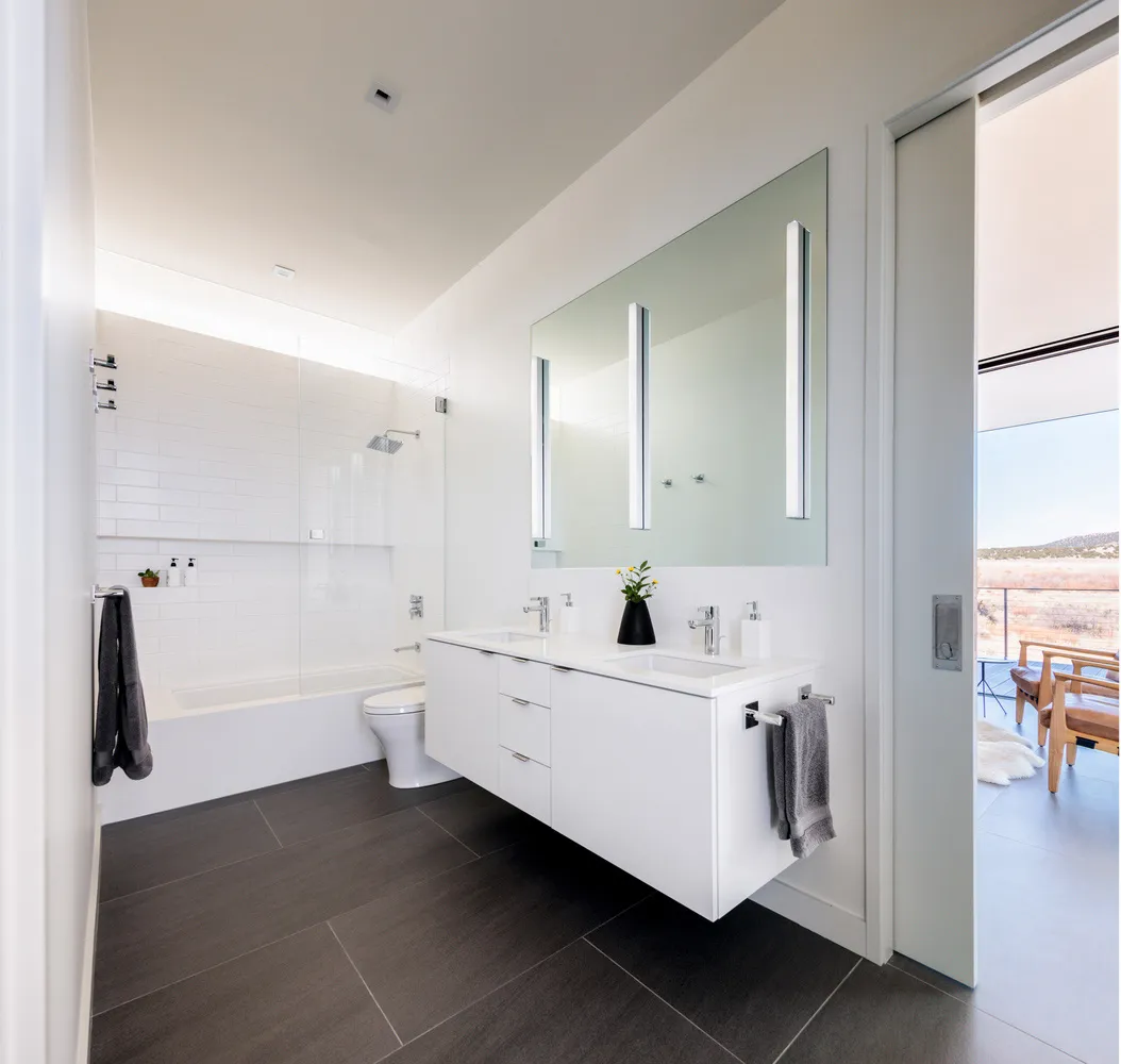 Modern bathroom with a white concrete countertop, black tile flooring, and a large mirror.