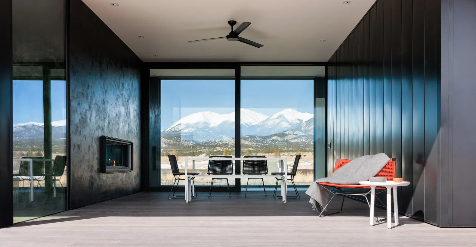 Modern living room featuring black-framed windows overlooking snowy mountains.