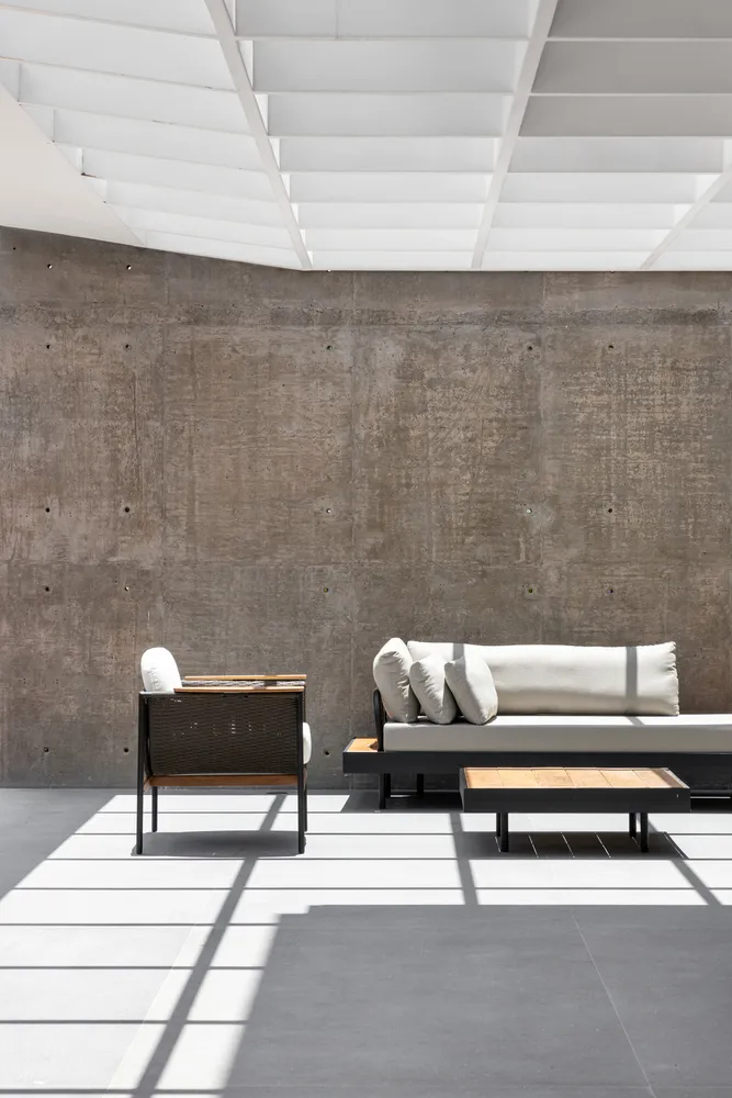 A modern minimalist living space featuring a concrete wall, wooden seating, and white cushions.