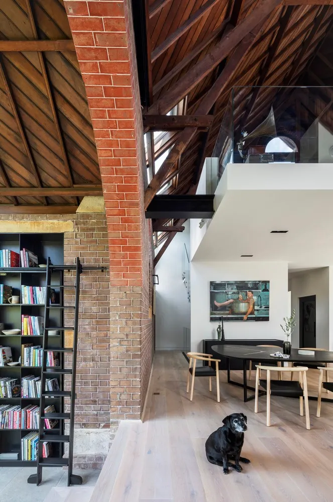 Modern residential space featuring exposed brick, concrete flooring, and wooden beams, with a black and white dog sitting on 