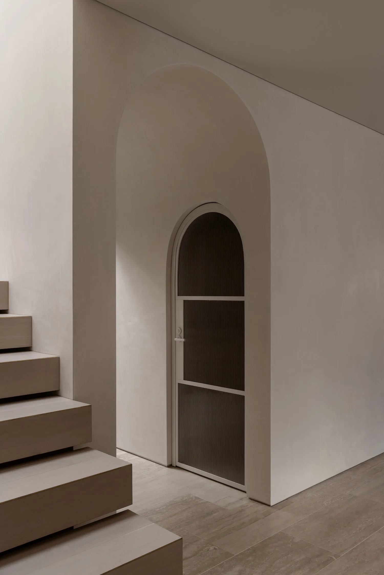 A minimalist entryway featuring concrete stairs and an arched doorway.