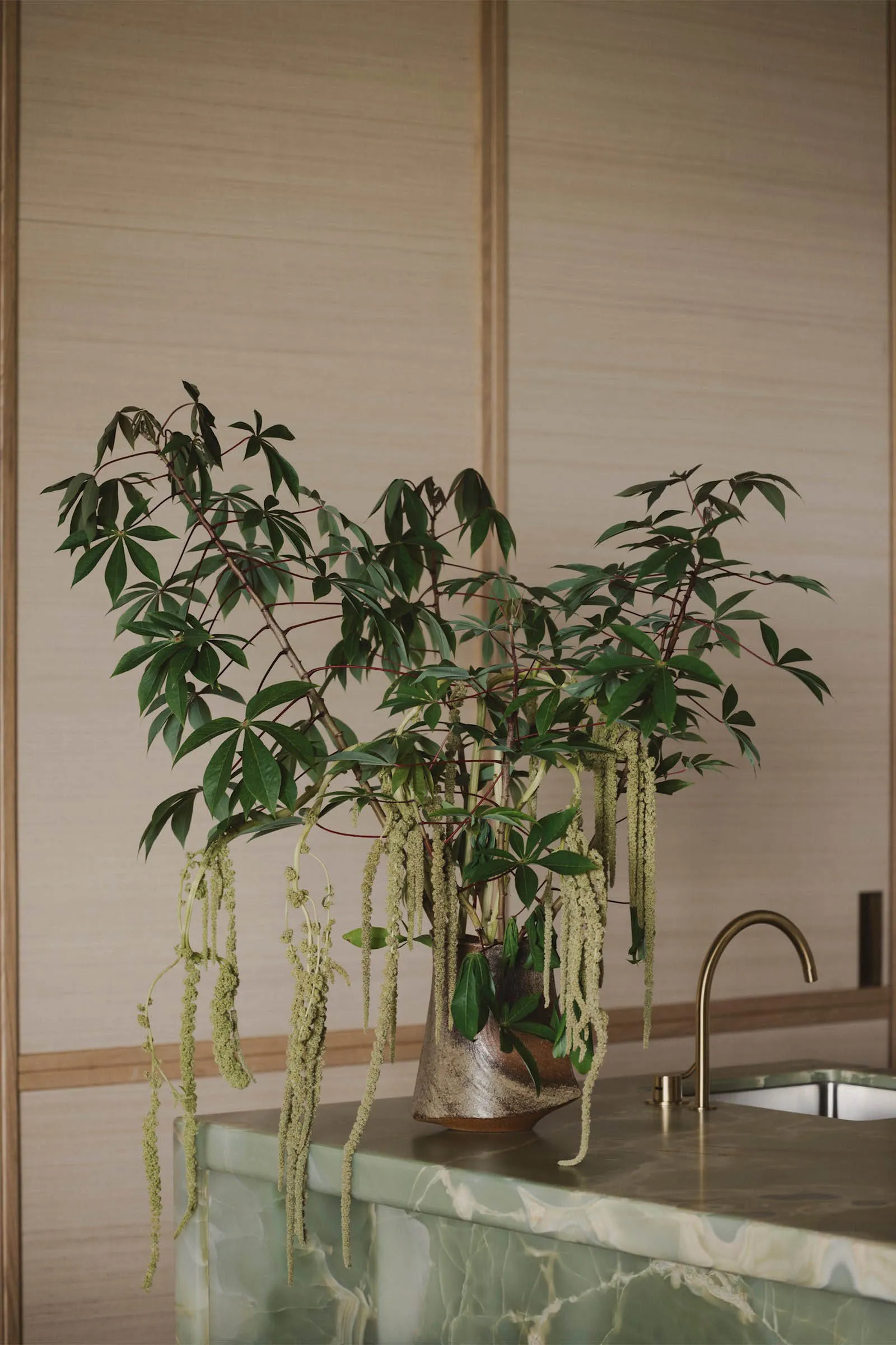 A modern kitchen interior featuring green marble countertops and a potted plant with green leaves and hanging flowers.