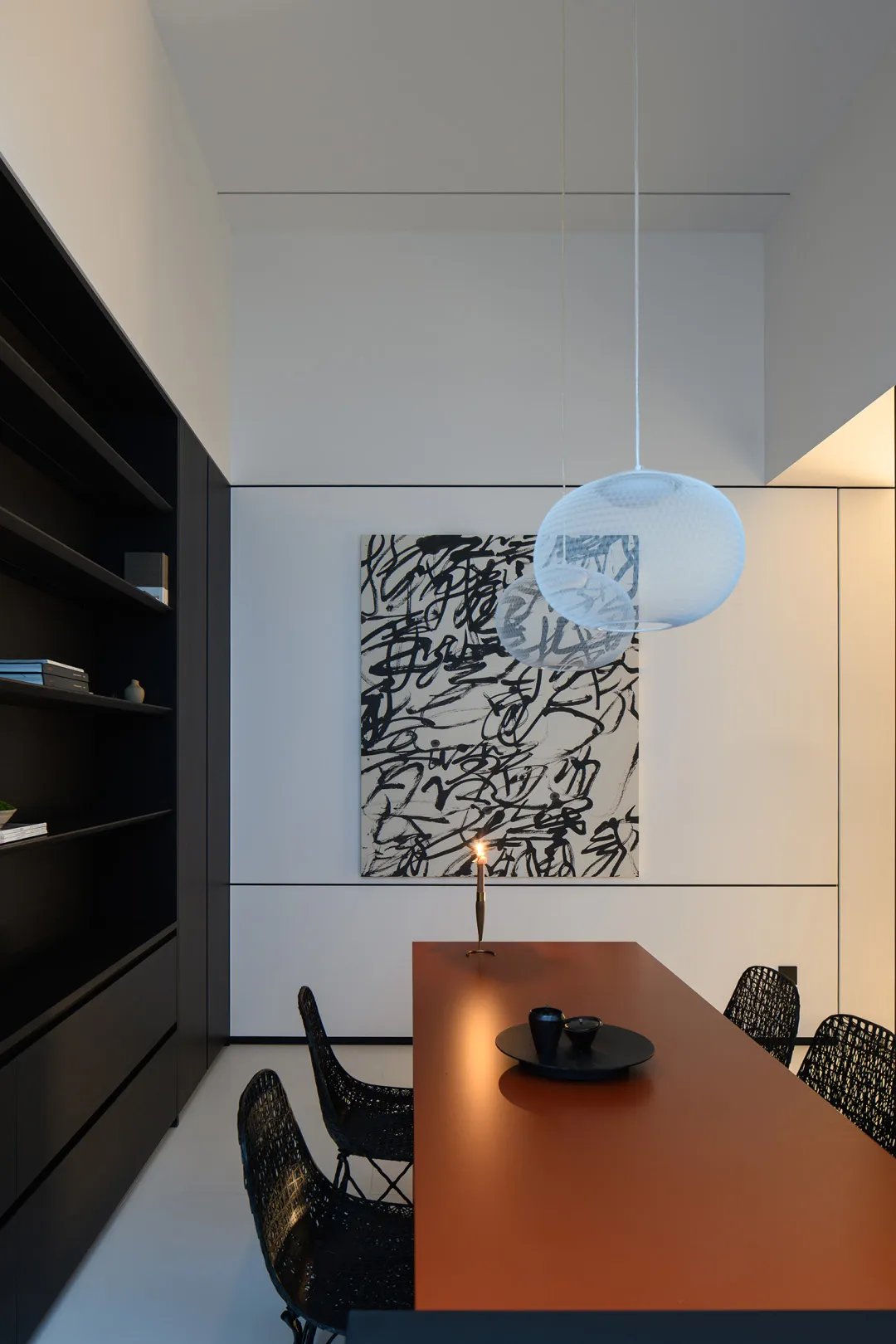 A modern minimalist dining space featuring a long brown table, black chairs, and a large abstract art piece on the wall.