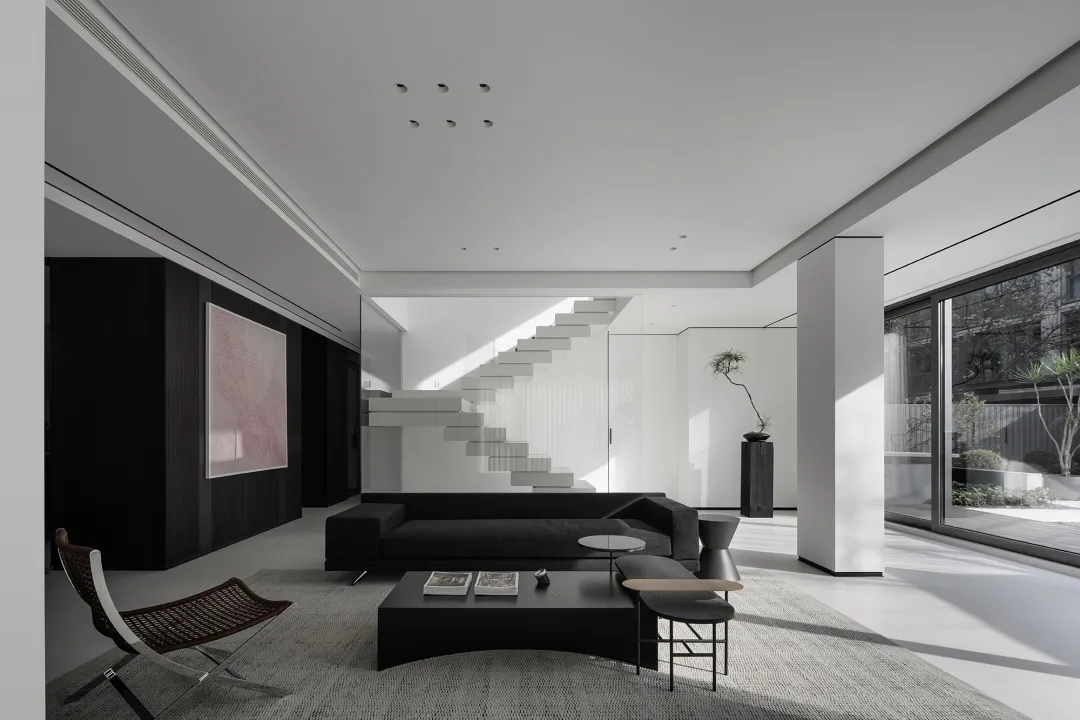Modern minimalist living room with concrete walls, glass doors, and metal accents.