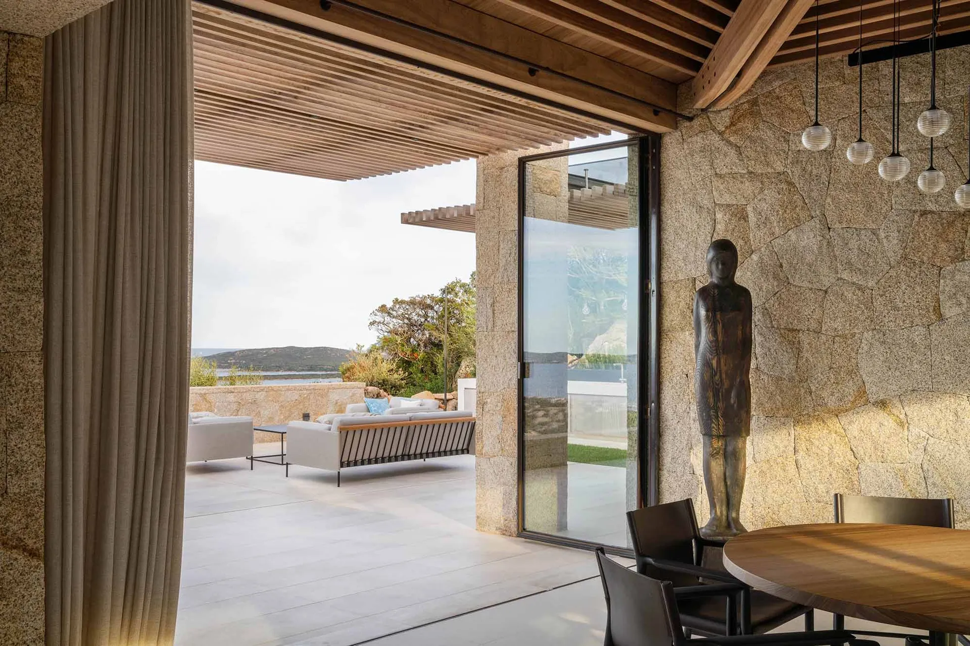 Modern residential exterior featuring granite walls, wooden ceiling beams, and glass doors.