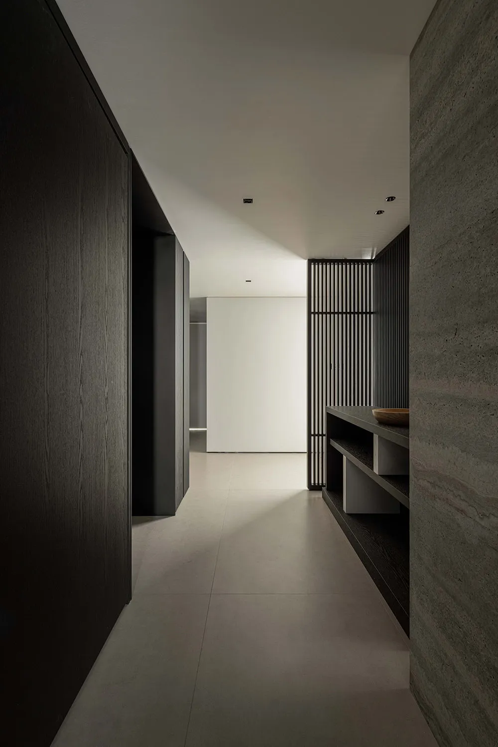 A minimalist corridor featuring concrete walls, dark wood accents, and metal fixtures, with a sleek, modern design.