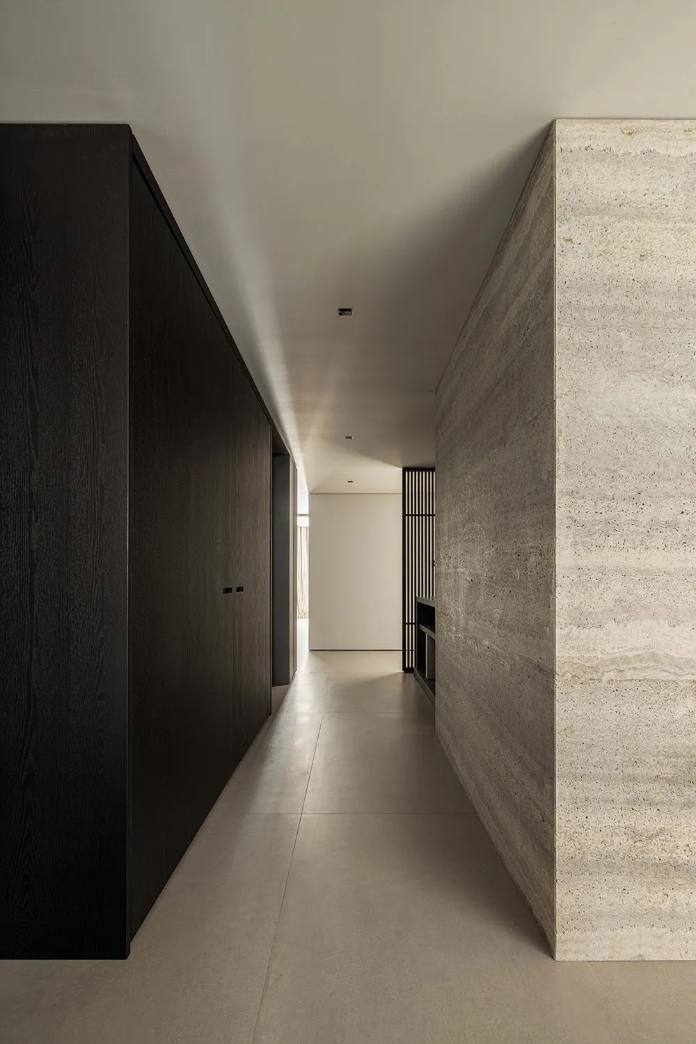 A modern, minimalist corridor featuring concrete walls and a metal chandelier with warm lighting.
