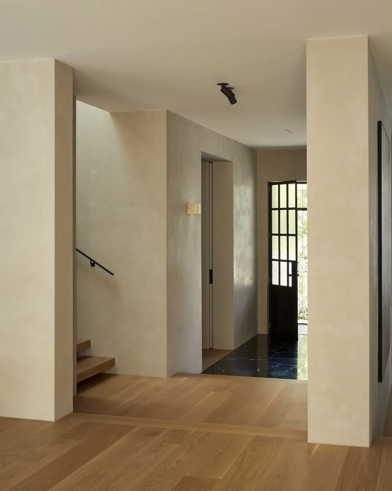 A modern minimalist entryway featuring light wood floors, concrete walls, and black metal accents.